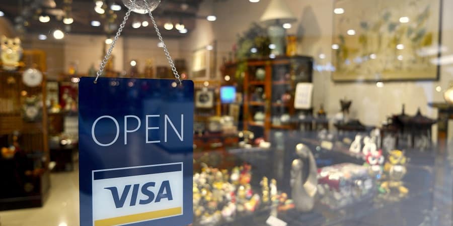 Pictured: the entrance to a storefront with a Visa sign on the door. Credit card companies, like Visa, add on surcharge fees to business credit card transactions that can be negated by offering a cash discount for purchases made. These savings on business expenses can quickly add up to meaningful money saved.